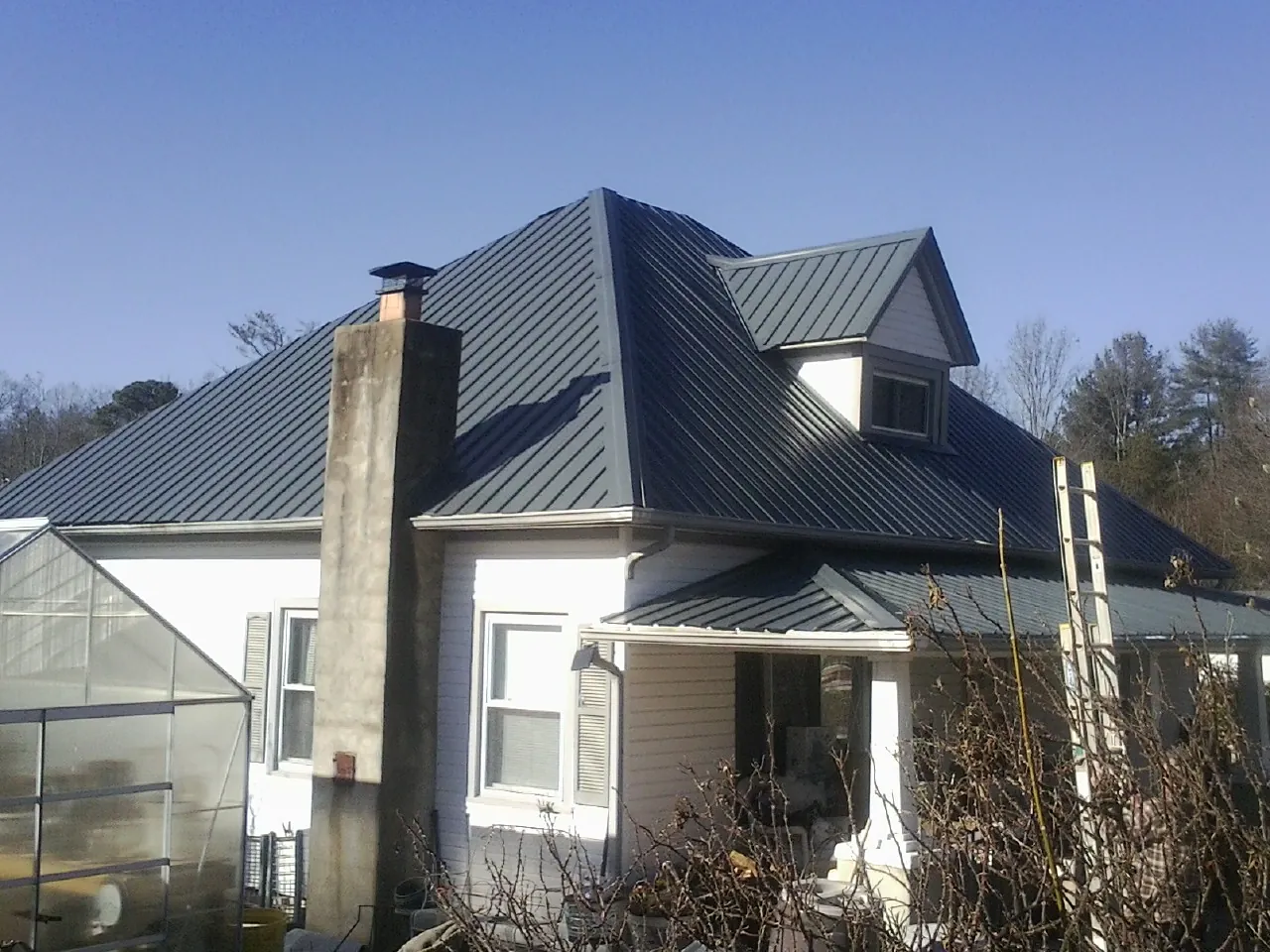 Dark blue standing seam metal roof on a white farmhouse with dormer — Slate & Tile Roof Repair by Roofing Brothers in Portal