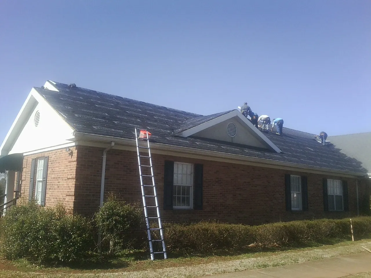 Crew tearing shingles off a brick ranch roof with a ladder set — Metal Roof Repair work by our crew in Portal