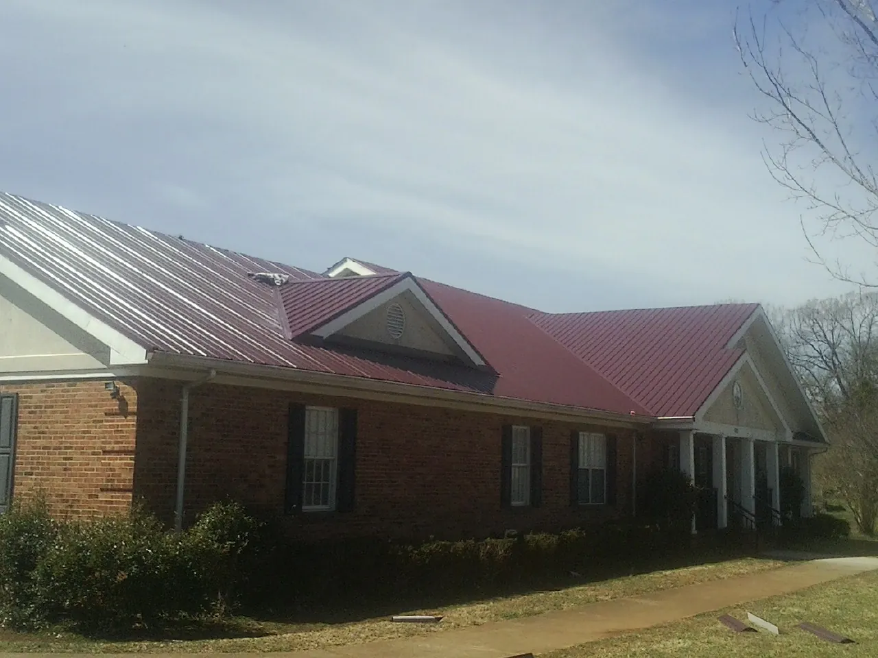 Red metal roof with gabled entries on a long brick building, from a Hail Damage Roof Repair job in Portal