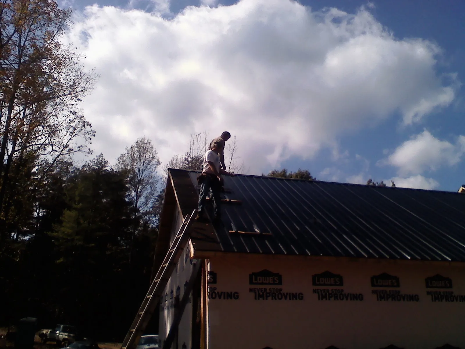 Roofer fastening dark metal panels high against a cloudy sky, from a Roof Inspection job in Portal