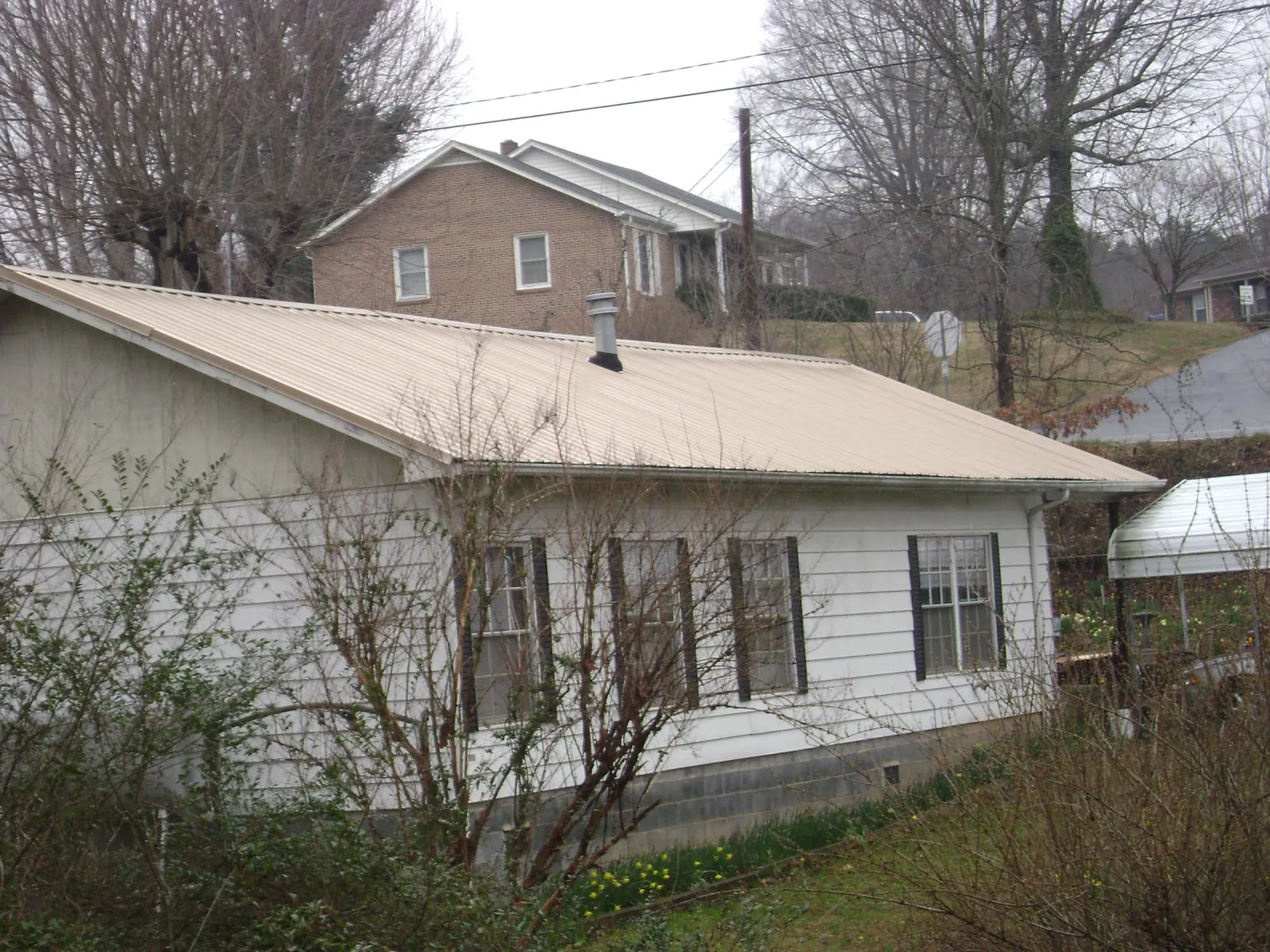 Tan metal roof on a white sided house set into a hillside — Commercial Roofing by Roofing Brothers in Portal